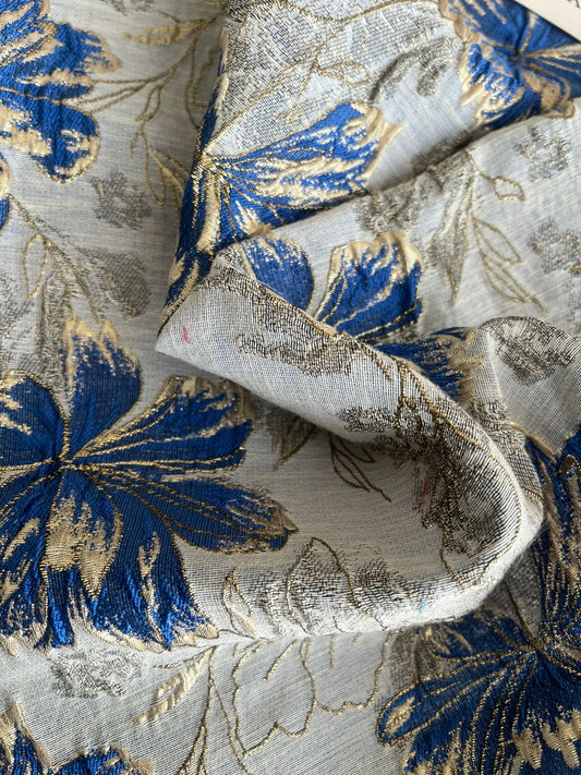 Jacquard floral blanco con flores azul rey y dorado, detalle de tela doblada