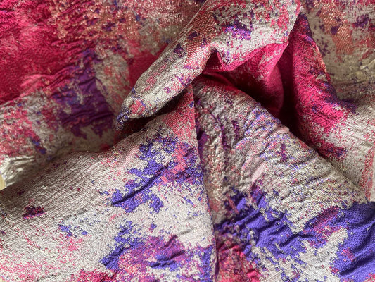 Tela jacquard metalizada dorada con estampado floral fucsia y morado, primer plano de textura brocada