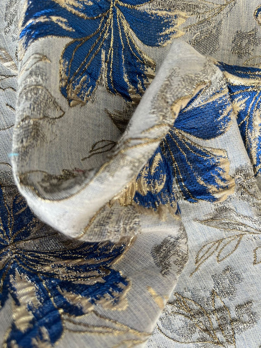 Jacquard floral blanco con flores azul rey y dorado, detalle de tela doblada